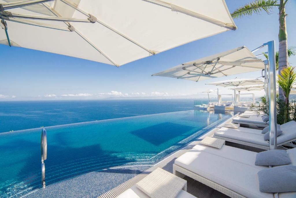 una piscina con tumbonas blancas y el océano en Hotel Mousai - Adults Only en Puerto Vallarta