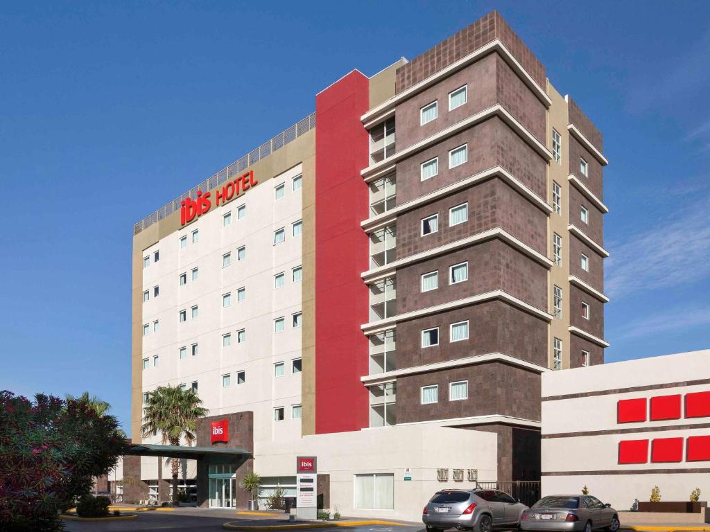 a tall red and white building with cars parked in front of it at Ibis Chihuahua in Chihuahua