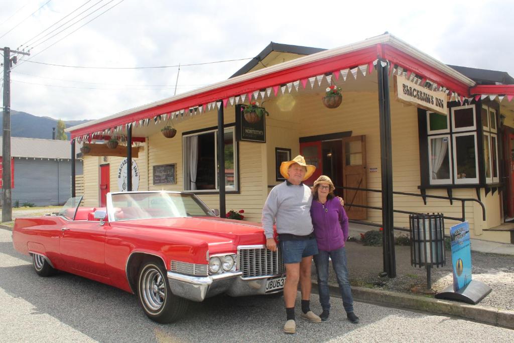 Um homem e uma mulher à frente de um carro vermelho. em Blackball's Inn & 08 Cafe em Blackball