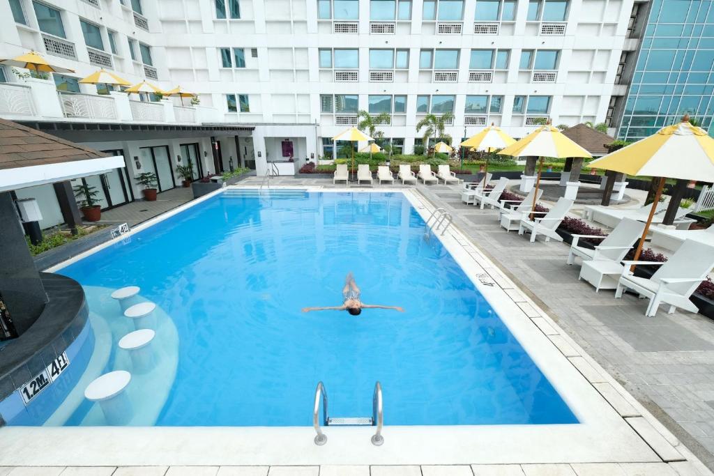 ein Pool in einem Hotel mit Stühlen und einer Person, die schwimmt in der Unterkunft Quest Hotel & Conference Center Cebu in Cebu City
