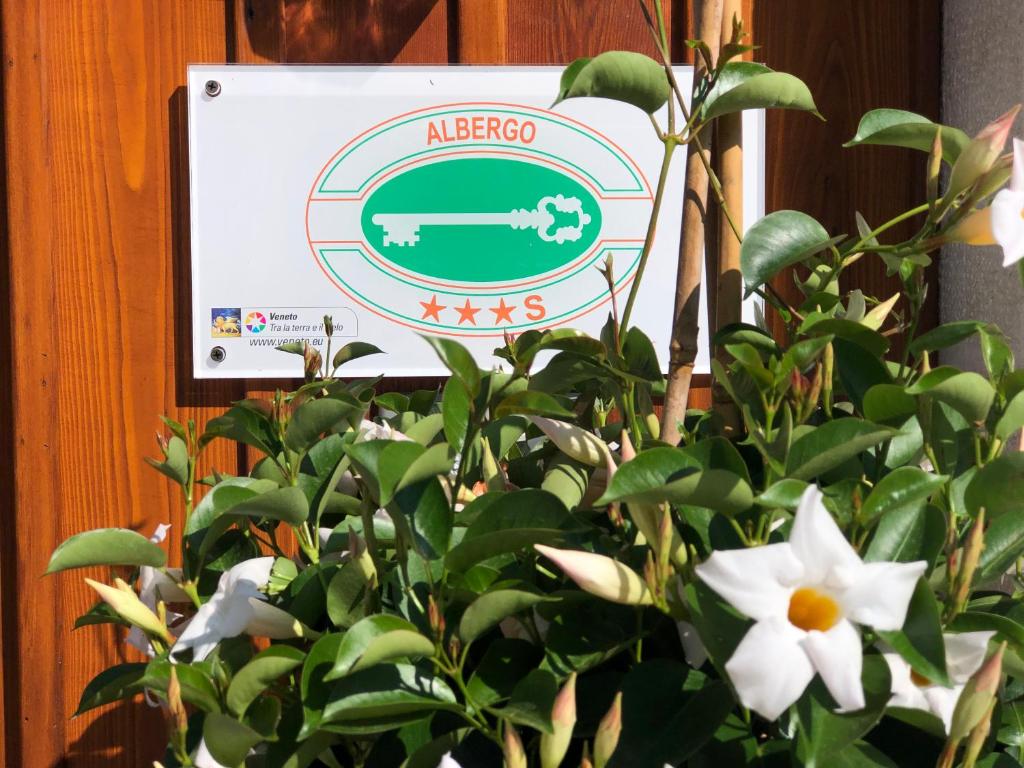 um sinal na parede ao lado de uma planta com flores brancas em Hotel Vecchia Stazione Mountain Elegance em Roana