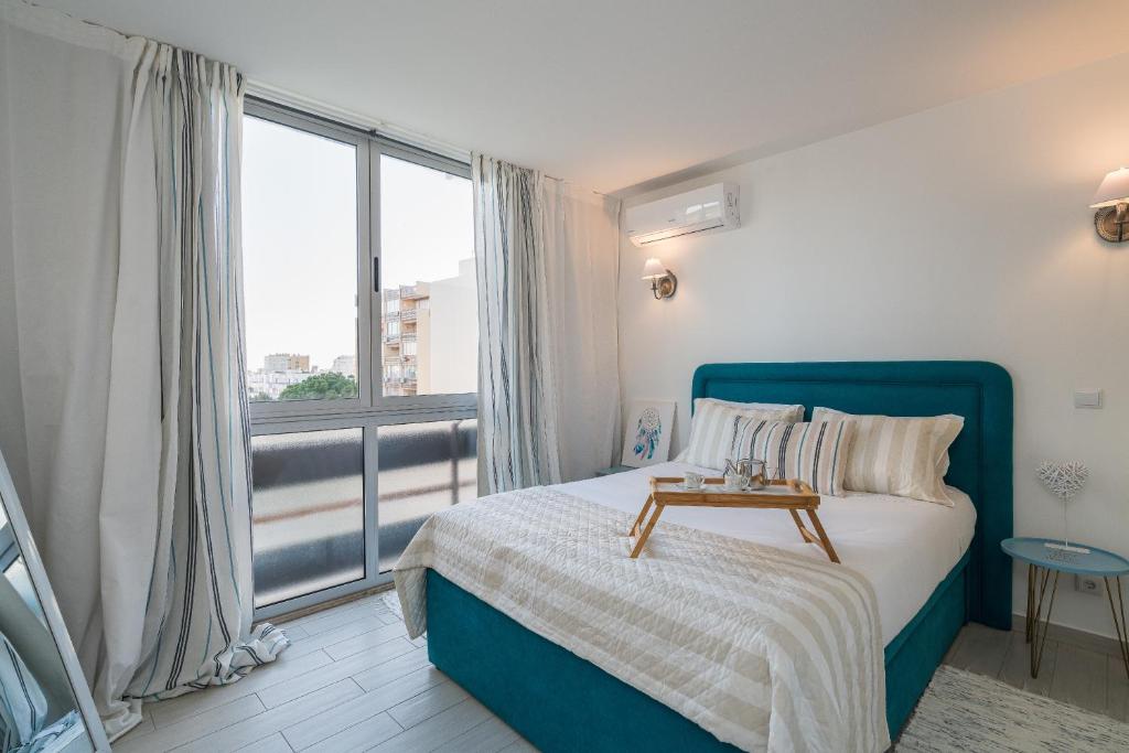 Un dormitorio con una cama azul y una gran ventana. en Serenity by the Marina, Vilamoura, en Quarteira