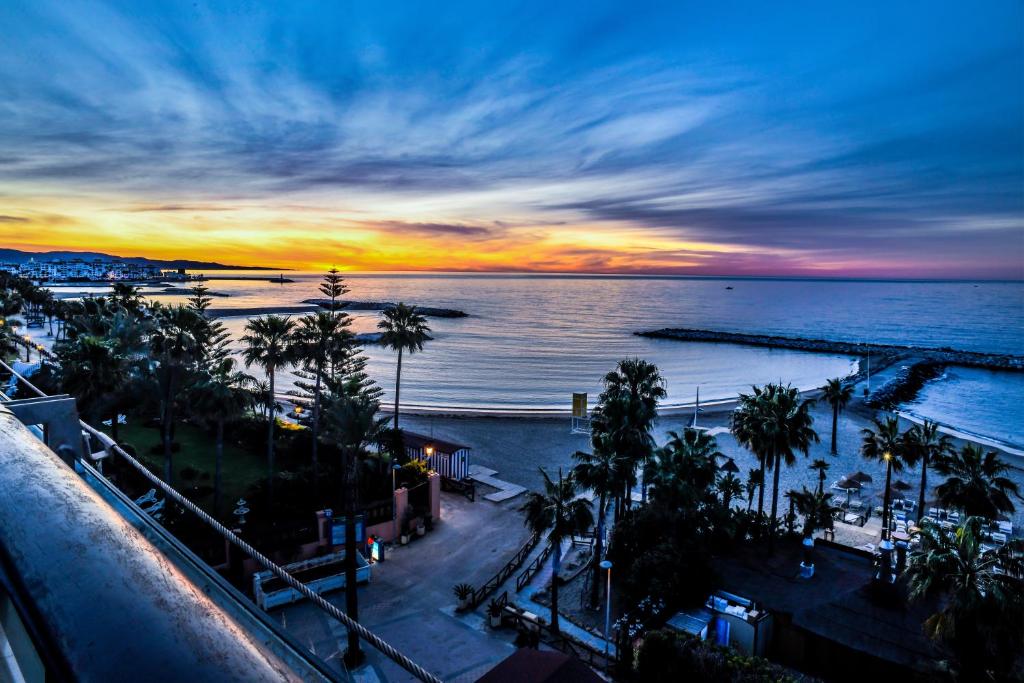 a sunset over the ocean and a beach with palm trees at Gran Hotel Guadalpín Banus in Marbella