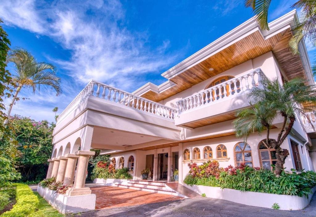 a large white house with a balcony and palm trees at Buena Vista Chic Hotel in Alajuela