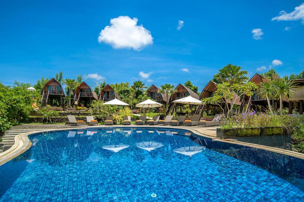 a pool at a resort with chairs and umbrellas at The Kirana Ungasan in Jimbaran