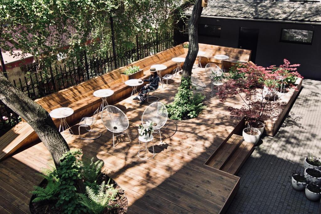 Sun-dappled wooden terrace with round tables, wire chairs, potted plants and single person seated.