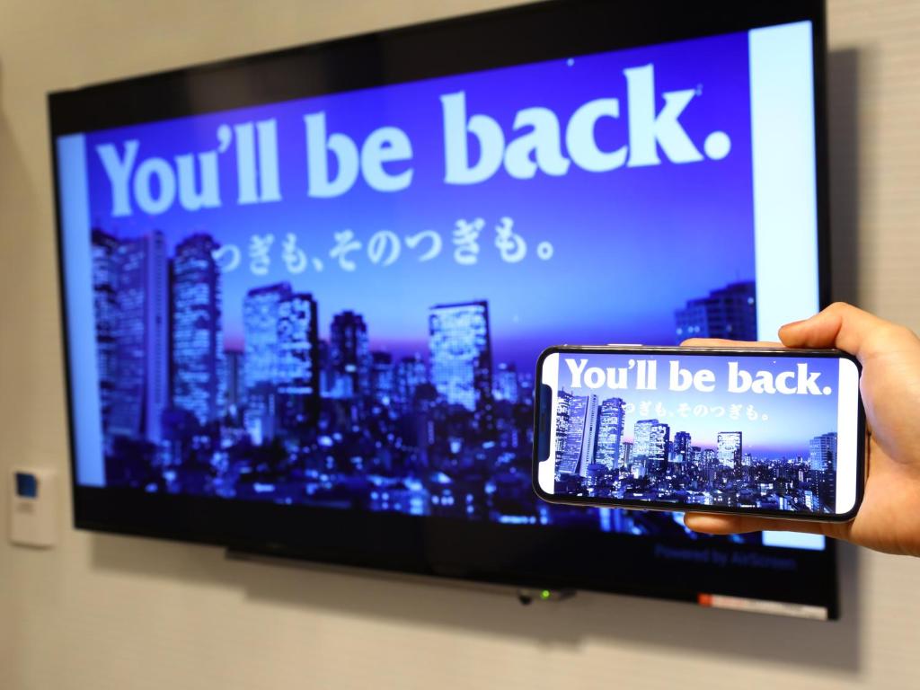 a person holding a cell phone in front of a tv at APA Hotel Ningyocho Ekikita in Tokyo