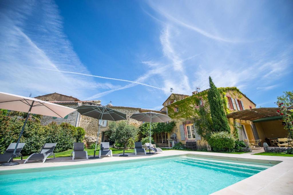 una piscina con sillas y sombrillas junto a una casa en La Demeure de Cybele - chambres d'hôtes en Drôme Provençale en Colonzelle