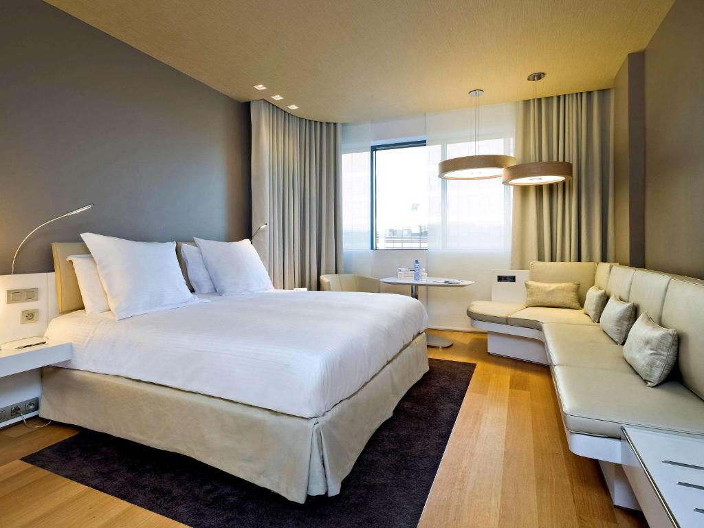 een slaapkamer met een groot wit bed en een bank bij Pullman Brussels Centre Midi in Brussel