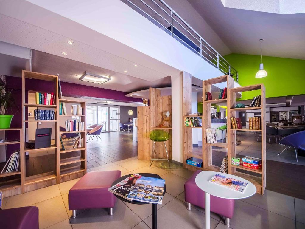 Habitación con estanterías, mesas y sillas moradas en ibis styles Brive Ouest, en Brive-la-Gaillarde