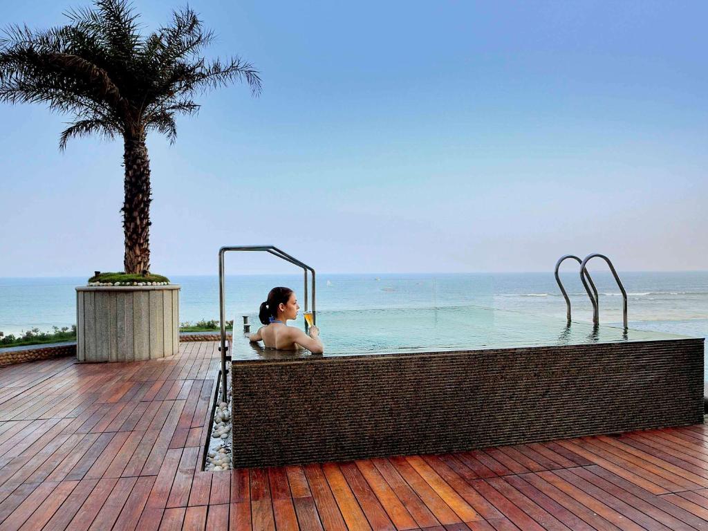 a woman sitting in a swimming pool next to the ocean at Novotel Visakhapatnam Varun Beach in Visakhapatnam