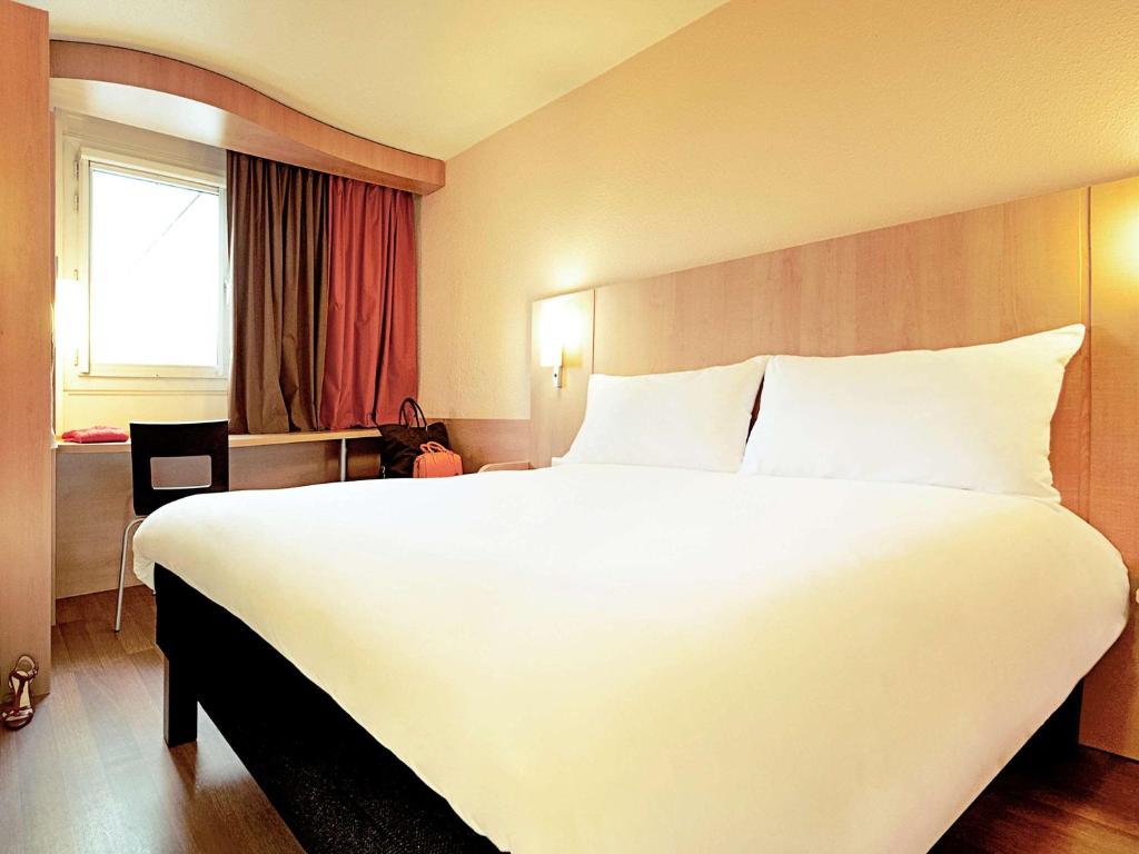 a large white bed in a hotel room with a window at Ibis Lleida in Lleida