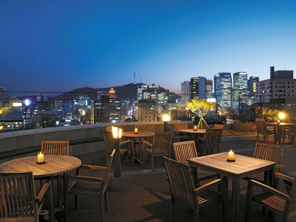 um pátio no último piso com mesas e cadeiras e um horizonte da cidade em ibis Ambassador Seoul Insadong em Seul