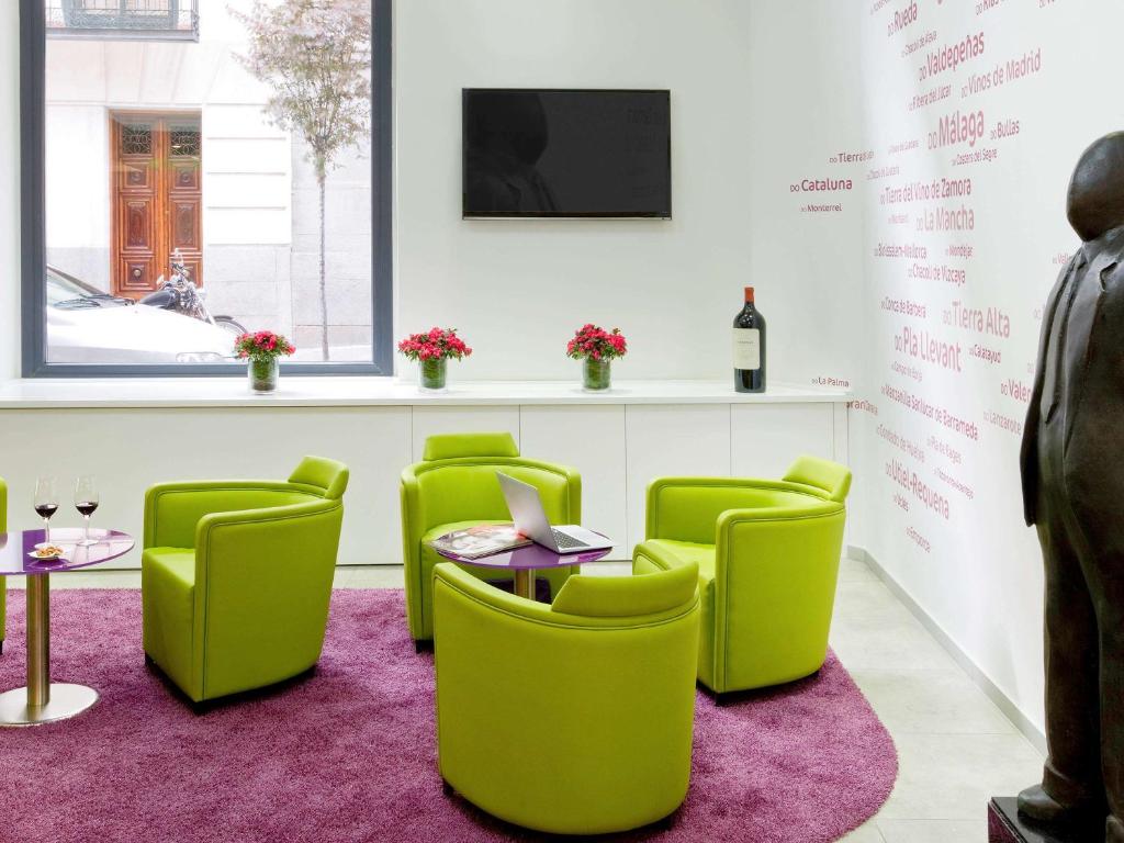 uma sala de espera com cadeiras verdes e uma mesa e uma televisão em Ibis Styles Madrid Prado em Madrid