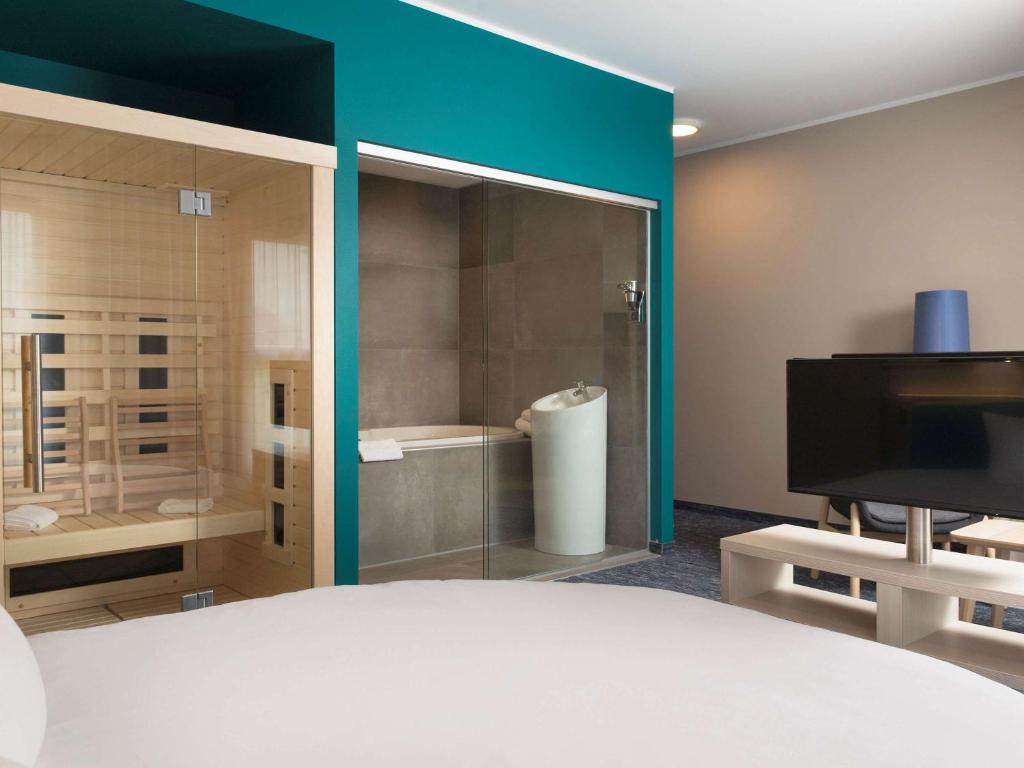 a room with a glass shower and a television at ibis Styles Nivelles in Nivelles