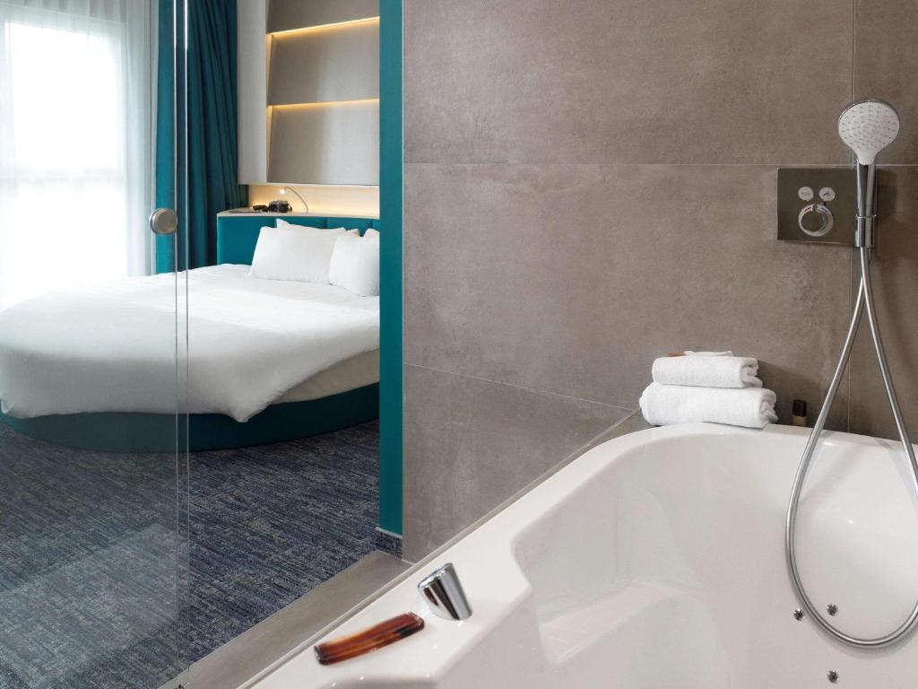 a bathroom with a bath tub and a bed at ibis Styles Nivelles in Nivelles