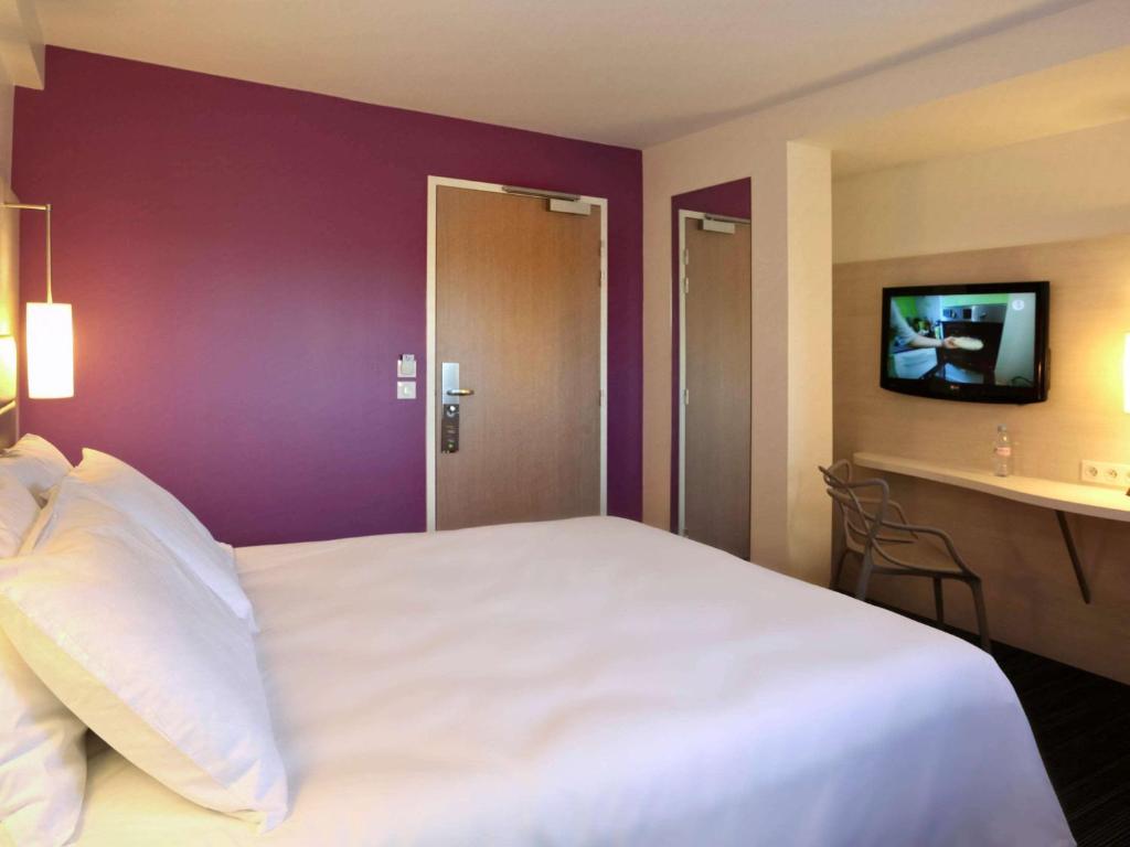 een slaapkamer met een groot wit bed met een paarse muur bij ibis Styles Quiberon Centre in Quiberon