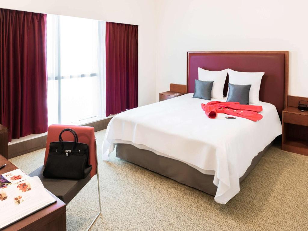 um quarto de hotel com uma cama grande com uma bolsa vermelha em Aparthotel Adagio Fujairah em Fujairah