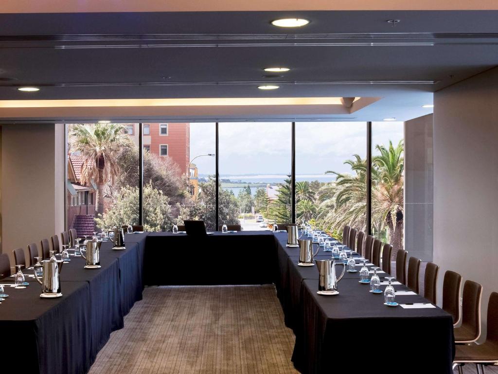 a conference room with tables and chairs and a large window at Novotel Newcastle Beach in Newcastle