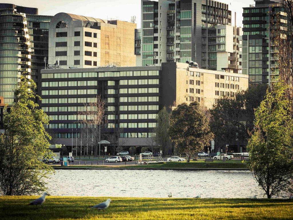 dos pájaros sentados en el césped frente a una ciudad en Mercure Melbourne Albert Park, en Melbourne