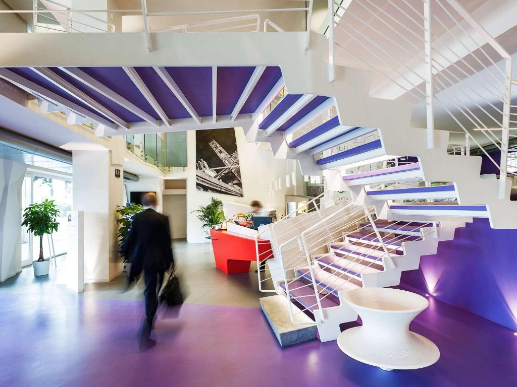 a person walking through a building with purple and white stairs at Ibis Styles Palermo President in Palermo
