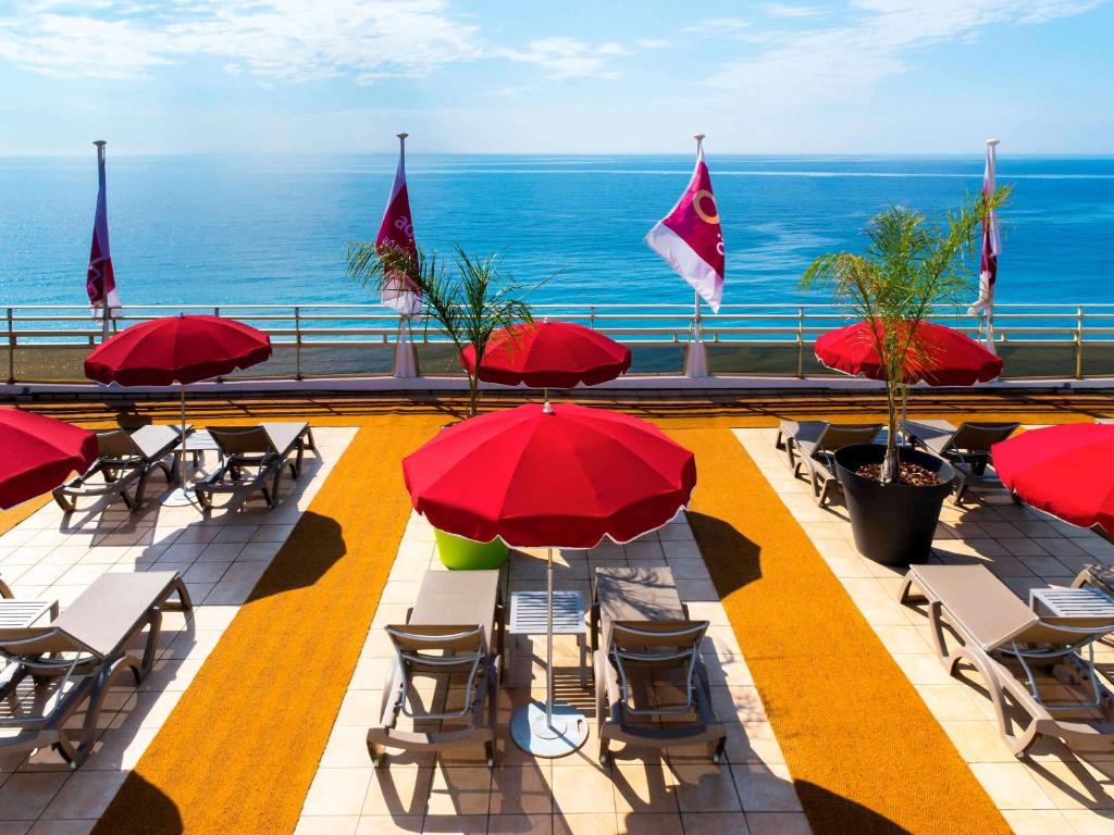 un patio avec des tables et des chaises et des parasols rouges dans l'établissement Aparthotel Adagio Nice Promenade des Anglais, à Nice