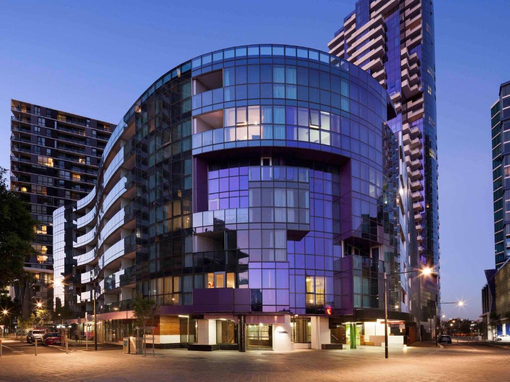 a large glass building in a city at night at The Sebel Melbourne Docklands Hotel in Melbourne