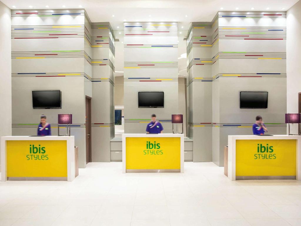 tres personas de pie detrás de los mostradores amarillos con las palabras "boletos de autobús" en Ibis Styles Jakarta Mangga Dua Square, en Yakarta