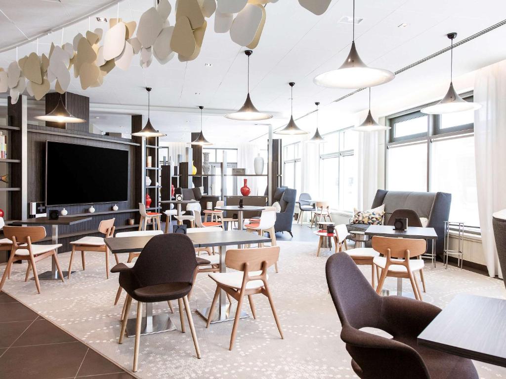 Cette chambre dispose de tables, de chaises et d'une télévision à écran plat. dans l'établissement Novotel Paris Saint Denis Stade Basilique, à Saint-Denis