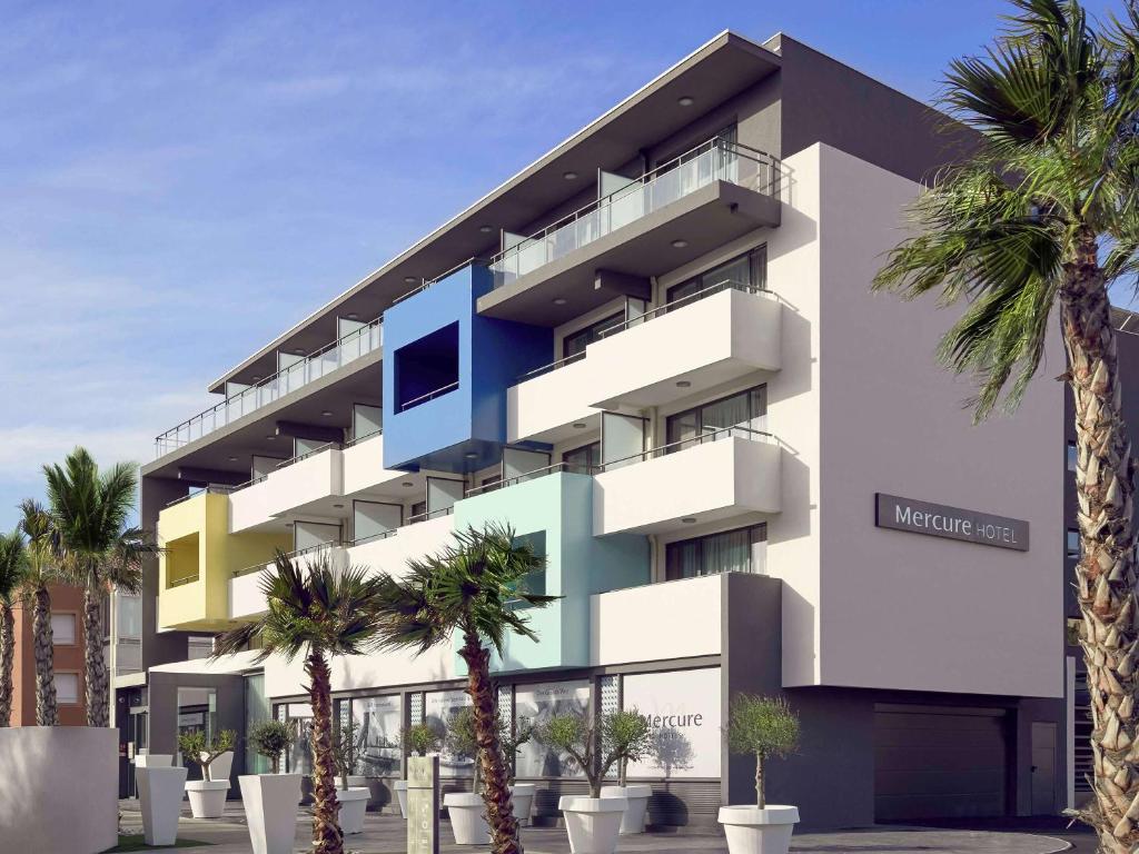 un bâtiment avec des palmiers en face de celui-ci dans l'établissement Mercure Hotel Golf Cap d'Agde, au Cap d'Agde