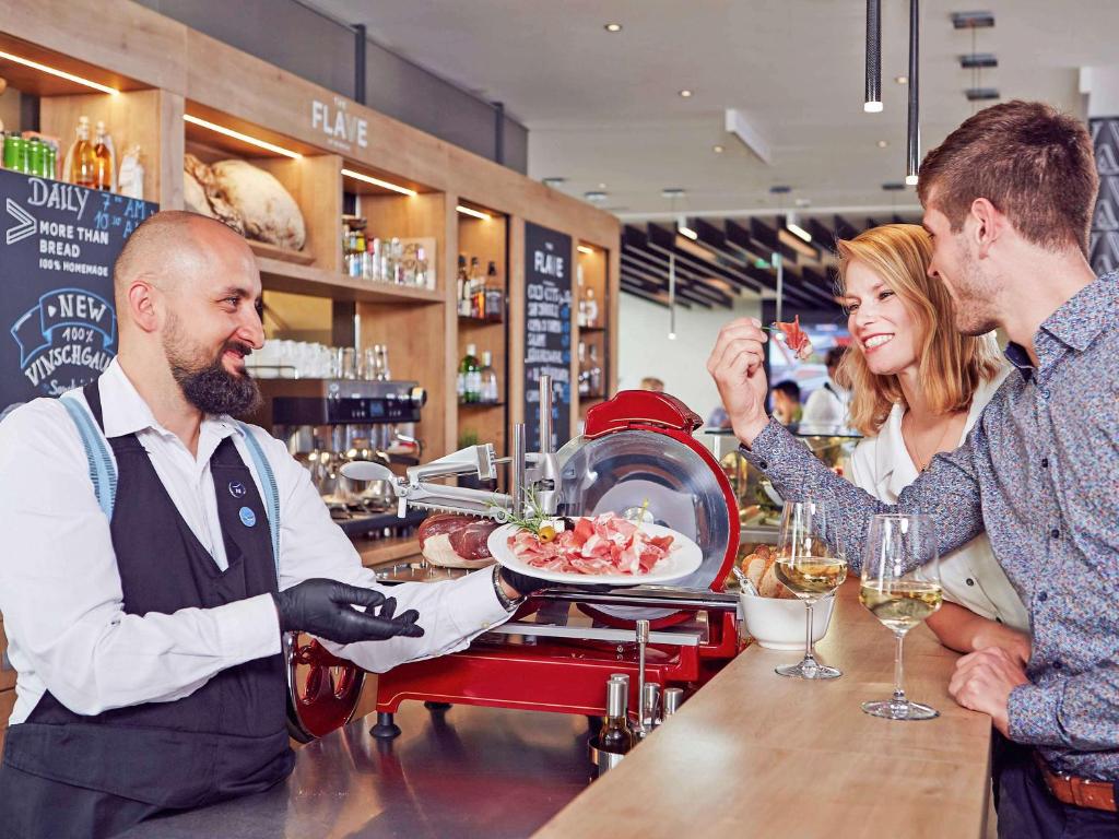 Eine Frau gibt einem Mann einen Teller Essen in einer Bar. in der Unterkunft Novotel München City Arnulfpark in München