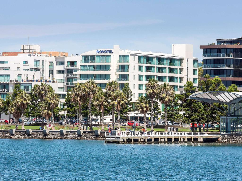 a large building with palm trees in front of a body of water at Novotel Geelong in Geelong