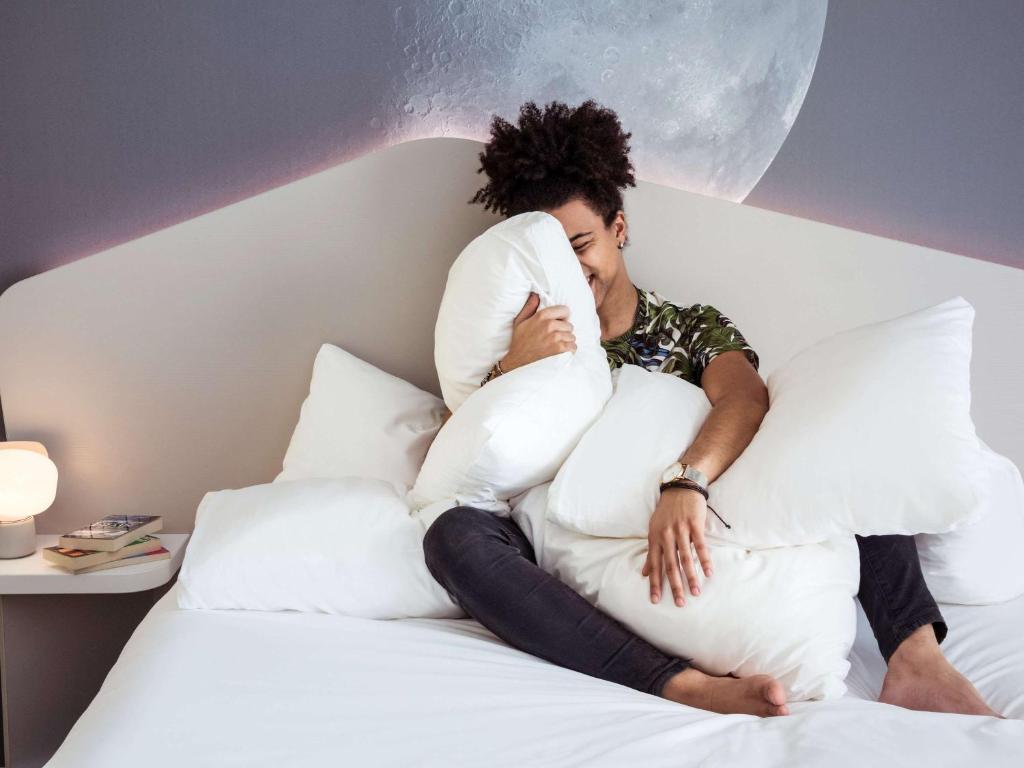 a man sitting on a bed with pillows at ibis Styles Paris Charles de Gaulle Airport in Roissy-en-France