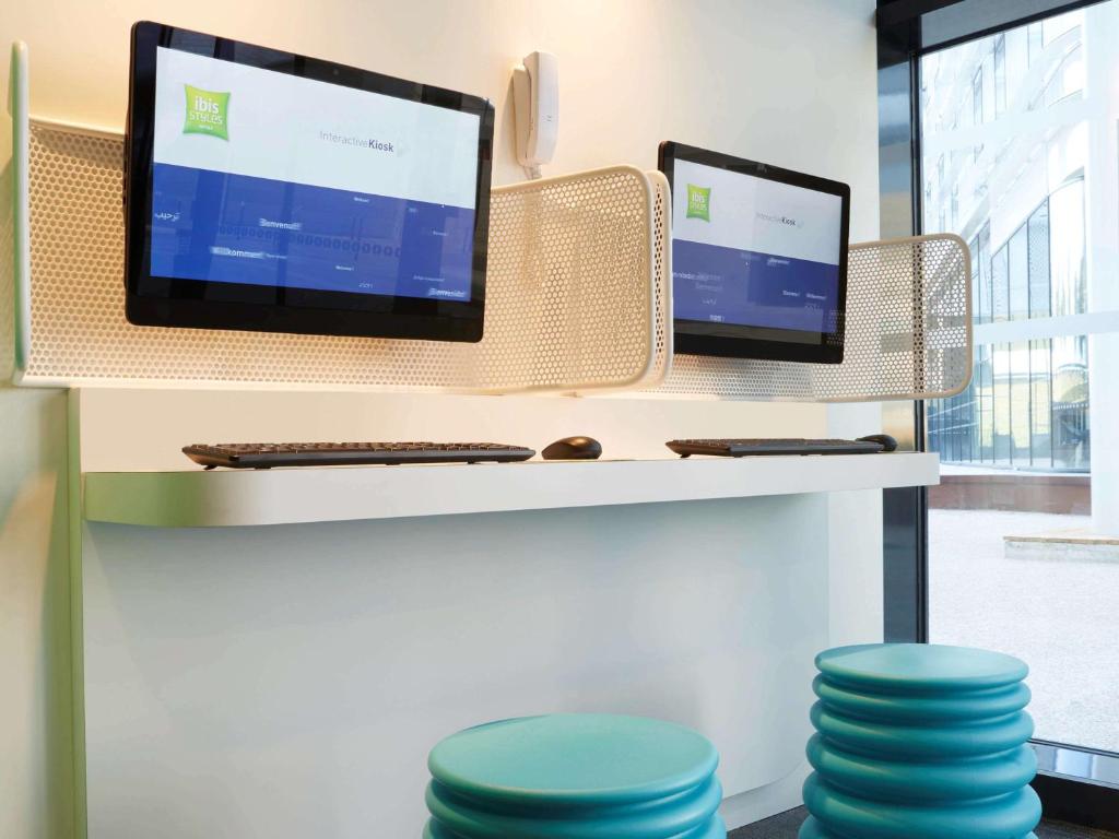 a desk with two monitors on a shelf with stools at ibis Styles Paris Charles de Gaulle Airport in Roissy-en-France