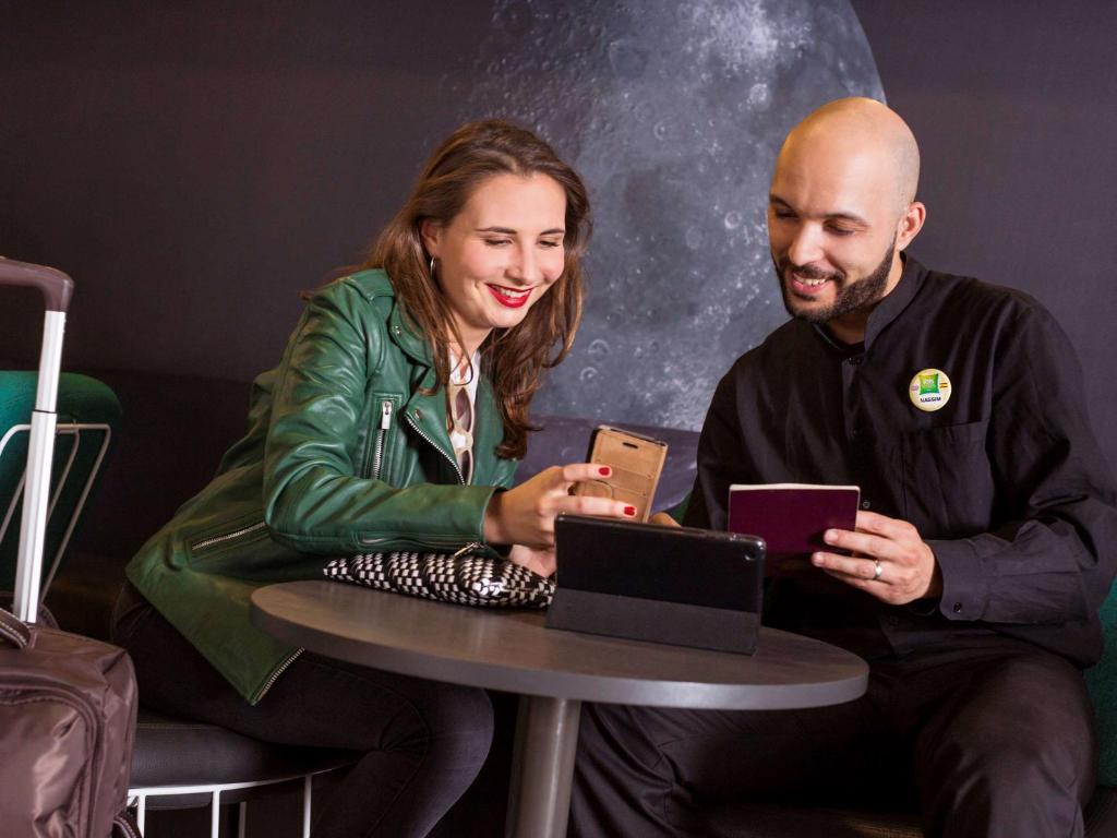 a man and a woman sitting at a table with a laptop at ibis Styles Paris Charles de Gaulle Airport in Roissy-en-France