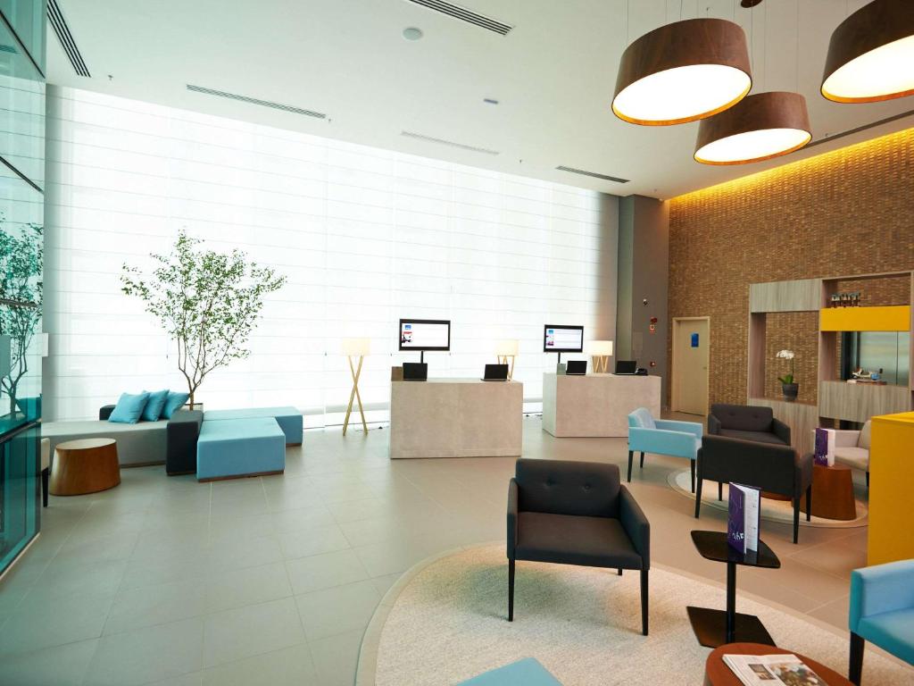 a lobby with a waiting room with chairs and tables at Novotel Santos Gonzaga in Santos