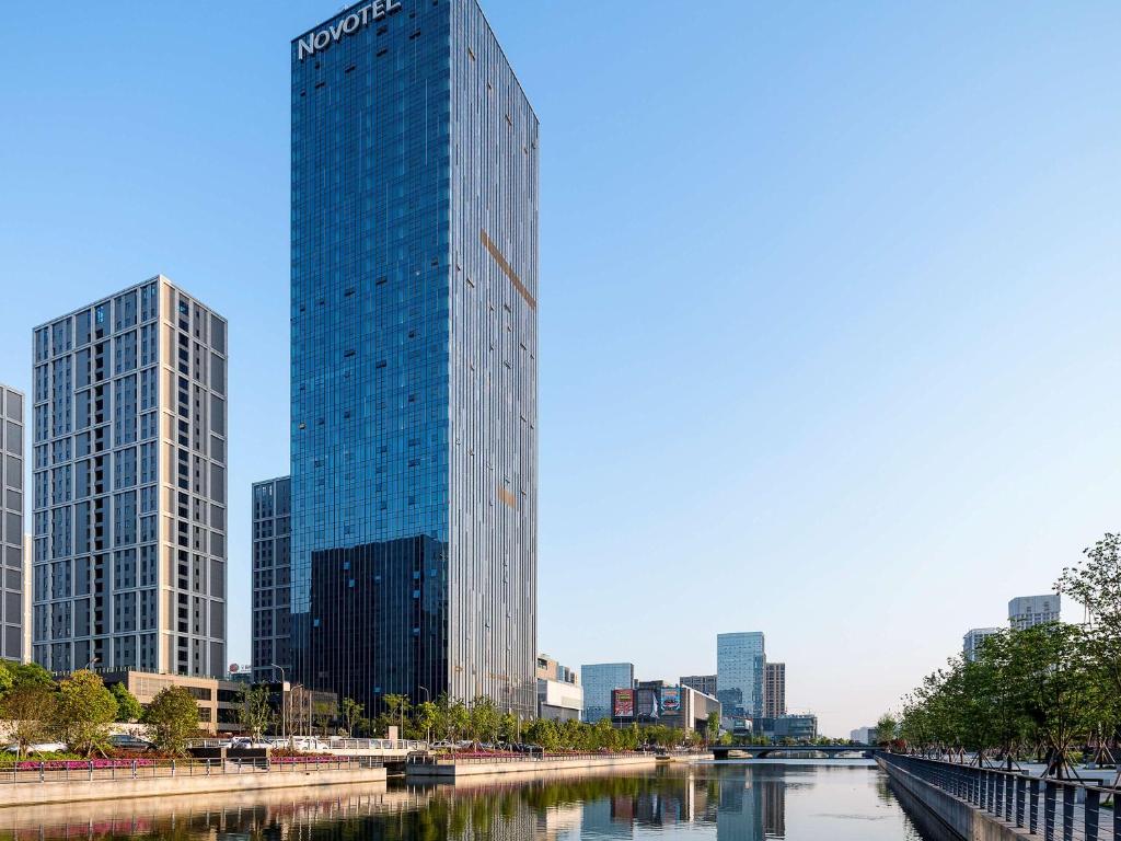 Novotel Ningbo East في نينغبو: مبنى زجاجي طويل بجوار جسم من الماء