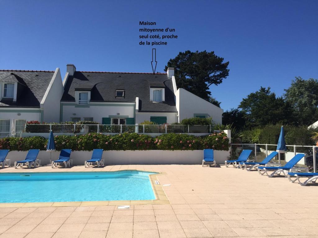 a pool with chairs and a building in the background at Maison de vacances de 56 m2 dans résidence avec piscine chauffée proche plages in Locmaria