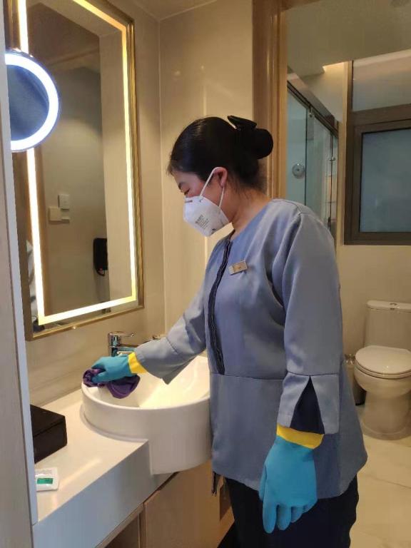 a woman wearing a mask washing a bathroom sink at Sincere Residence Changfeng - Changfeng Ecological Business District - Near Exit 3 of Changfeng Park Station on Subway Line 15 in Shanghai
