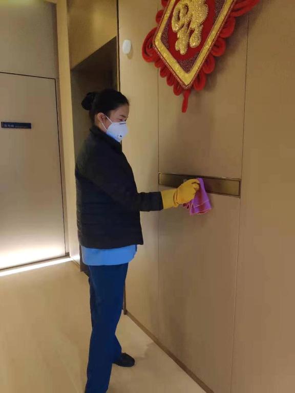 a woman wearing a face mask and yellow gloves opening a door at Sincere Residence Changfeng - Changfeng Ecological Business District - Near Exit 3 of Changfeng Park Station on Subway Line 15 in Shanghai
