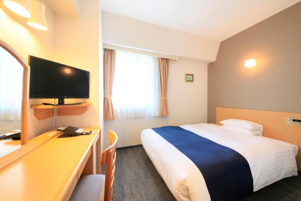 um quarto de hotel com uma cama e uma secretária com uma televisão em Hotel Grand City em Tóquio