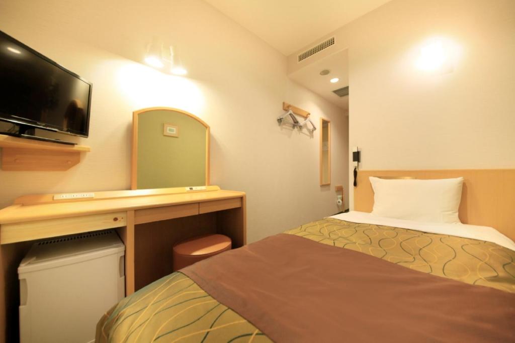 a hotel room with a bed and a desk with a tv at Hotel Grand City in Tokyo