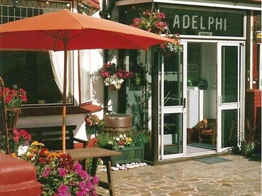 een rode paraplu voor een winkel met een tafel bij The Adelphi in Paignton