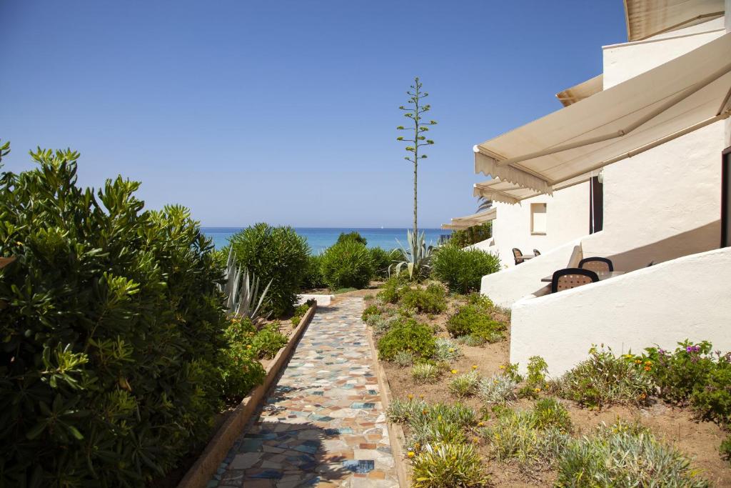 a walkway next to a house with the ocean in the background at Hôtel et Résidence Ta Kladia - Omigna in Cargèse