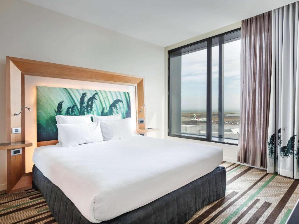 a large white bed in a room with a large window at Novotel Auckland Airport in Auckland