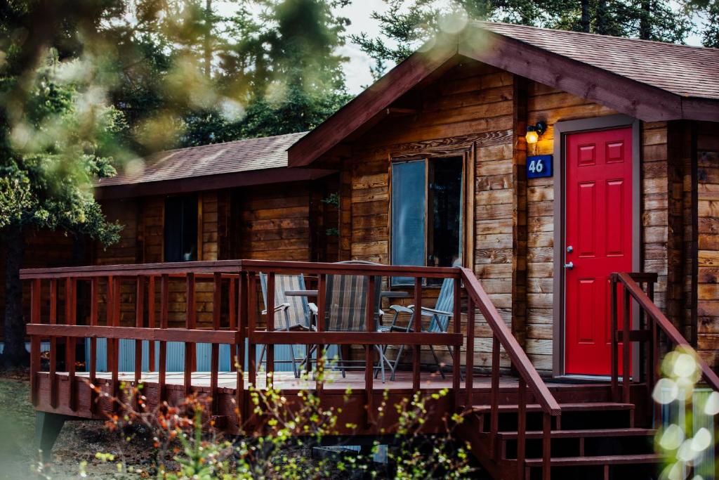 a log cabin with a red door and a deck at Denali Cabins in McKinley Park