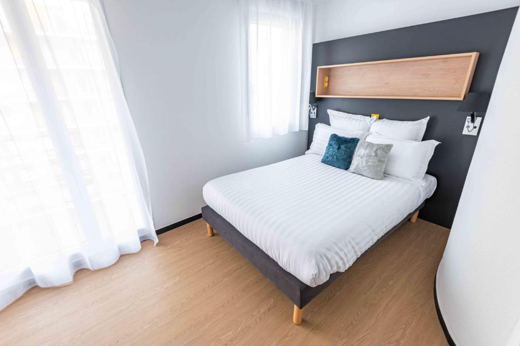 um quarto com uma cama com lençóis brancos e almofadas azuis em Apparthotel Le Hüb Grenoble em Grenoble