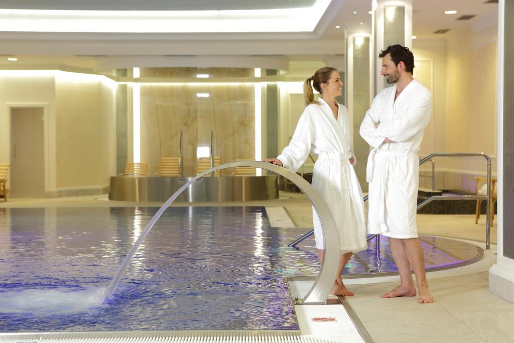 Un uomo e una donna in piedi accanto a una piscina di Parkhotel Richmond a Karlovy Vary