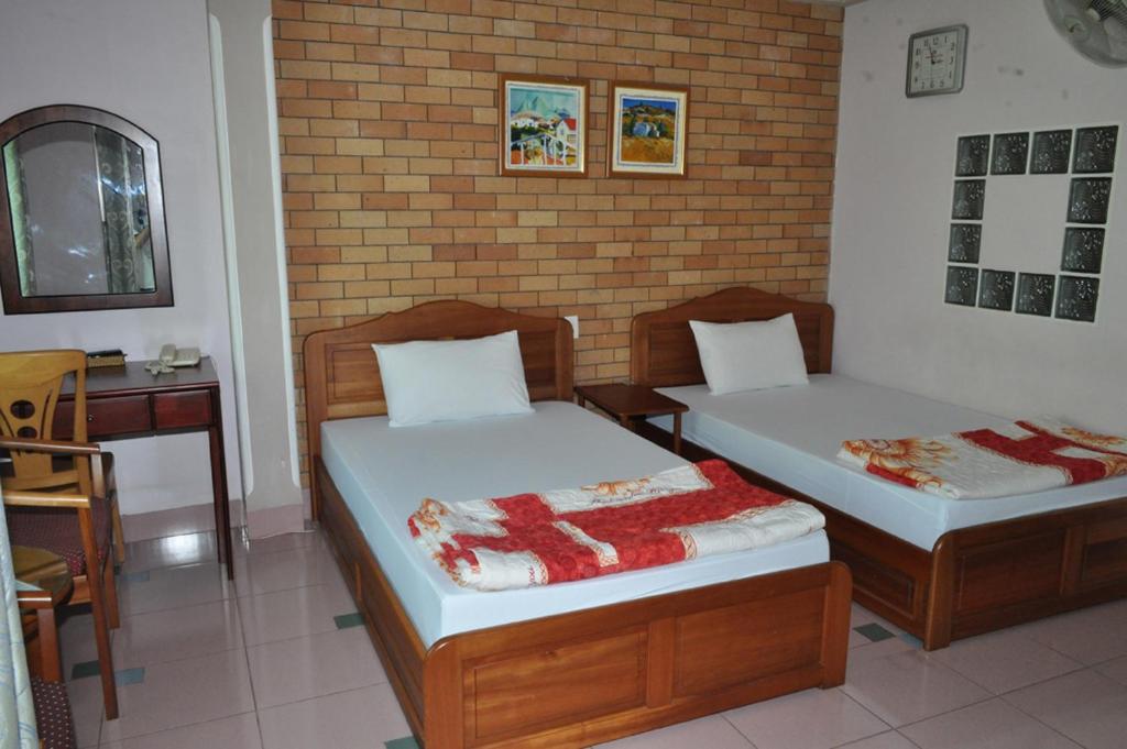 two beds in a room with a table and a desk at An An Hotel in Rạch Giá