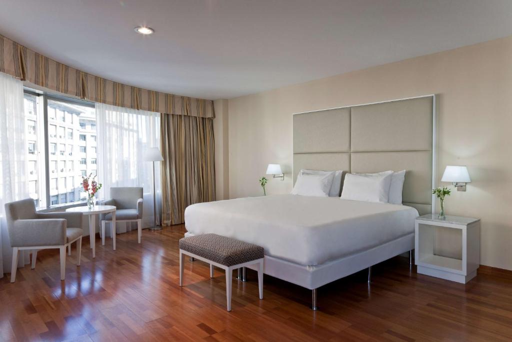 een slaapkamer met een groot wit bed en 2 tafels en stoelen bij NH Buenos Aires Latino in Buenos Aires